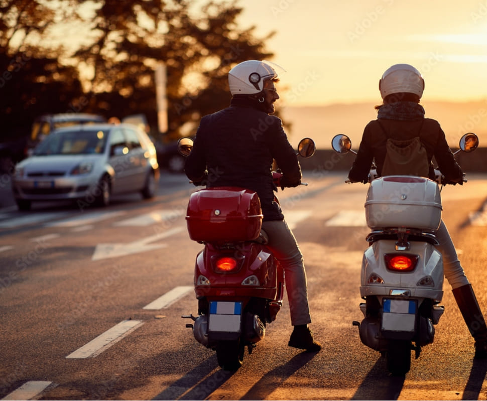 Deux scootéristes casqués à l’arrêt sur une route au coucher du soleil
