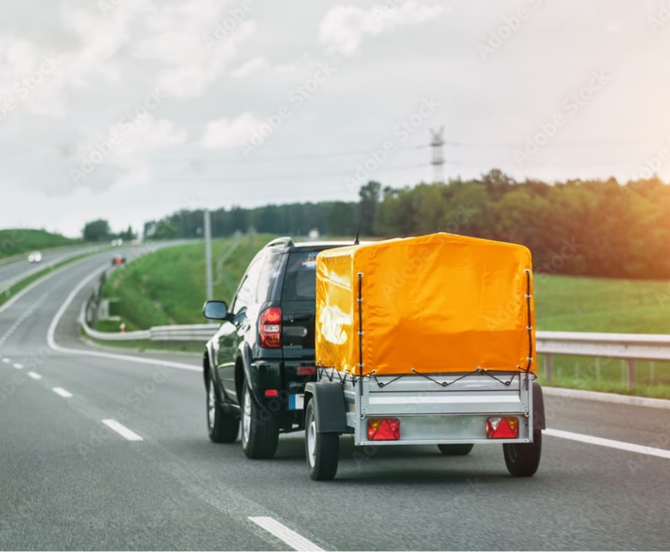 Un 4x4 tractant une remorque bâchée jaune sur une route de campagne