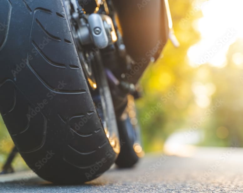 Roue arrière d’une moto à l’arrêt, au ras du sol, à contre-jour